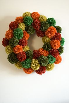 a multicolored pom - pom wreath hangs on the wall in front of a white background