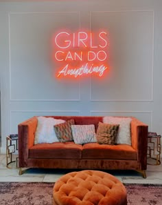 a couch and ottoman in front of a neon sign that says girls can do anything