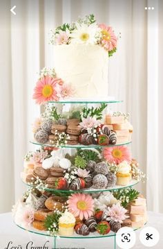 a three tiered cake with flowers and cookies on the top is surrounded by greenery