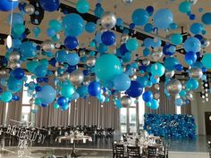 blue and silver balloons hanging from the ceiling in a banquet hall with tables set up for an event