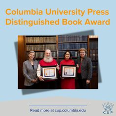 three women and one man holding up a framed book in front of bookshelves