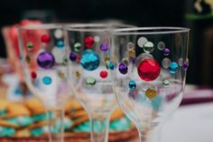 three wine glasses with colorful beads on them are sitting on a table next to cookies