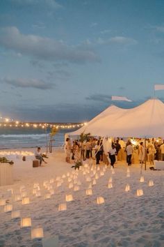 a group of people standing on top of a beach next to a white tent covered in paper lanterns