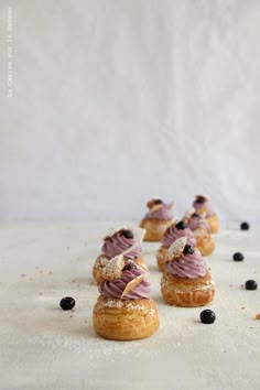 small pastries with purple icing and blueberries on a white surface