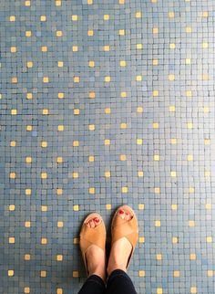 a woman's feet with sandals on standing in front of a blue tiled floor