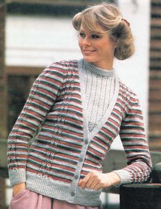 a woman standing next to a fence wearing a striped sweater and pink pleated skirt