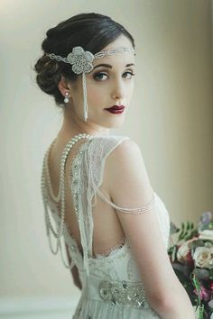 a woman in a white dress holding a bouquet and wearing a head piece with pearls on it