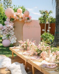 a table set up for a baby shower with balloons and flowers on the back wall