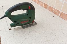 a green electric sander sitting on top of a white tile floor next to a tiled wall