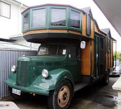 an old green truck parked in front of a building with a spiral staircase on the roof