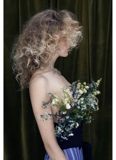 a woman with curly hair holding flowers in her hand