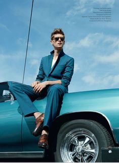 a man sitting on the back of a green car in front of a blue sky