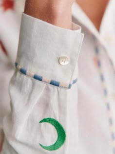 a close up of a person's hand wearing a white shirt with green crescent embroidered on it