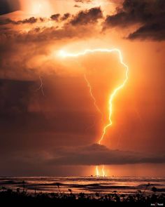 a large cloud with lightning coming out of it and some water in the foreground