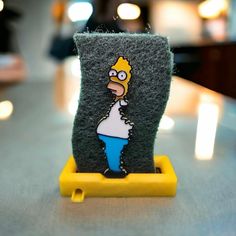 the simpsons phone case is sitting on top of a yellow stand with an image of homer