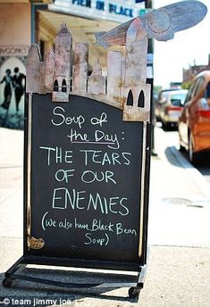 a sign on the sidewalk that says soup of the day, the tears of our enemes we also have black beans