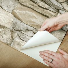 a person is cutting out a piece of paper on top of a wooden table next to a stone wall