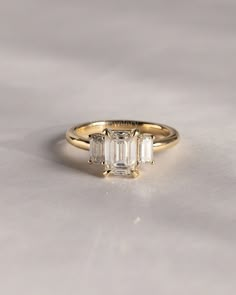 a three stone ring with an emerald cut diamond in the center and two smaller baguettes on each side