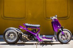 a purple motorcycle parked on the side of a road next to a yellow wall and some concrete