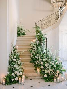 an elegant staircase decorated with white flowers and greenery, candles and chandelier