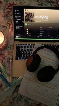 an open laptop computer sitting on top of a bed next to a candle and notebook