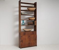 a tall wooden shelf with bowls and vases on it's sides, against a white wall