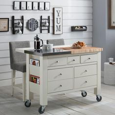 a kitchen island with two chairs and a cutting board on the top, in front of a white wall