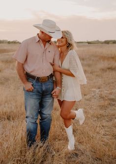 a man and woman standing in the middle of a dry grass field with their arms around each other