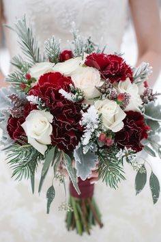 a bride holding a bouquet of red and white flowers with greenery in her hands