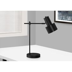 a black desk lamp sitting on top of a white table in front of a window