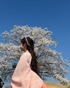 a woman standing in front of a blooming tree with her back to the camera