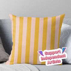 a yellow and pink striped pillow with the words support independent artists on it, sitting on a couch