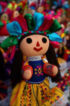 a stuffed doll is wearing a colorful dress and headdress, with many other dolls in the background