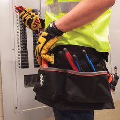 a man in yellow safety vest holding tool belt with many tools and wires inside it