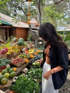 a woman standing in front of a table filled with lots of fruits and veggies