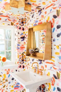 a sink and mirror in a room with colorful wall paper on the walls, gold faucet