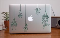 an apple laptop sitting on top of a wooden table next to a potted plant