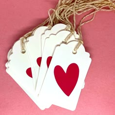 four white tags with red hearts hanging from twine on pink tablecloth, closeup