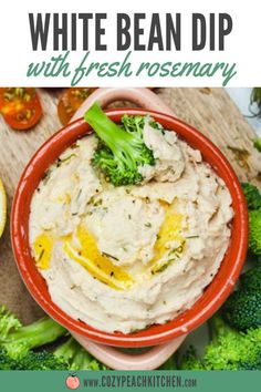 white bean dip with fresh rosemary in a red bowl surrounded by broccoli and lemons