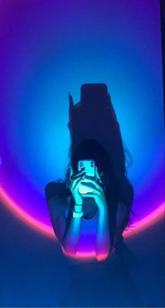 a woman taking a photo with her camera in front of a neon light tunnel that is blue and purple