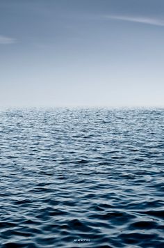 the ocean is very blue and calm with some clouds in the sky above it,