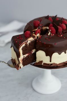 a chocolate cake with white frosting and raspberries on top is cut in half