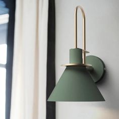 a green wall light mounted on the side of a white wall next to a window