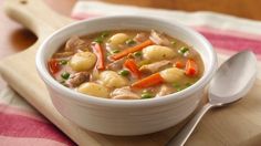 a bowl of chicken and dumpling soup on a wooden cutting board with a spoon