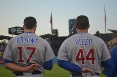 two baseball players in grey jerseys standing on the field with their backs to each other