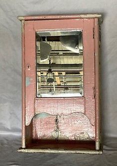 an old pink wooden clock on a white sheeted tablecloth covered wall behind it is a broken window