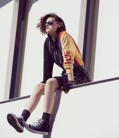 a woman sitting on top of a metal rail with her legs crossed and wearing black sneakers