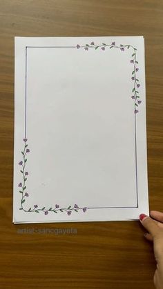 a person holding up a piece of paper with purple flowers on the bottom and green leaves above it