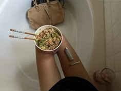 a person sitting in a bathtub holding a bowl of cereal and two pencils