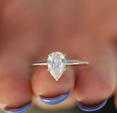 a woman's hand holding a ring with a pear shaped diamond on it